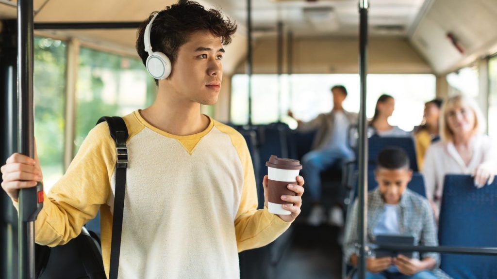 バスでコーヒーを飲みながら音楽を聴いているアジアの男性